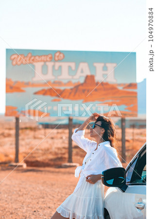 Beautiful woman on her trip by the car on the background of Welcome to Utah state border sign right in the Monument Valley 104970884