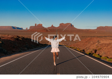 Happy young woman in white dress on the famous road to Monument Valley in Utah. Amazing view of the Monument valley. Happy young woman in white dress on the famous road to Monument Valley in Utah. Amazing view of the Monument valley. 104970904
