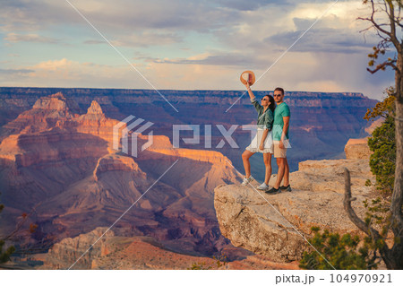 Happy young couple on a steep cliff taking in the amazing view over famous Grand Canyon on a beautiful sunny day, Grand Canyon National Park, Arizona, USA Happy young couple on a steep cliff taking in the amazing view over famous Grand Canyon on a beautiful sunny day, Grand Canyon National Park, Arizona, USA 104970921