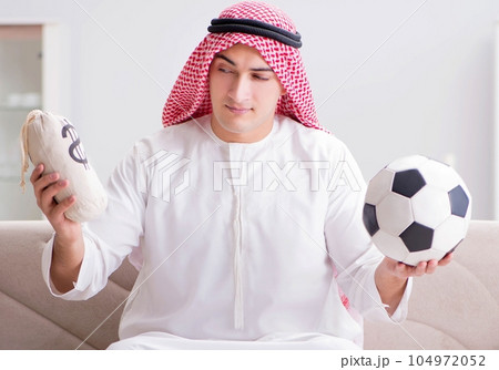 Young arab man watching football sitting on sofa Young arab man watching football sitting on sofa 104972052