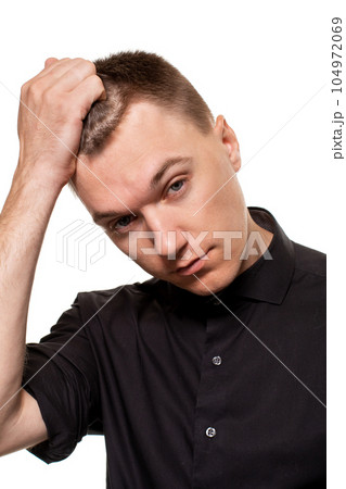 Handsome young man in a black shirt is making faces, while standing isolated on a white background Handsome young man in a black shirt is making faces, while standing isolated on a white background 104972069