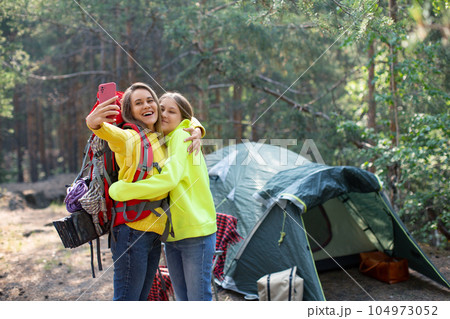 Mom with daughter taking a selfie in a forest camp. 104973052