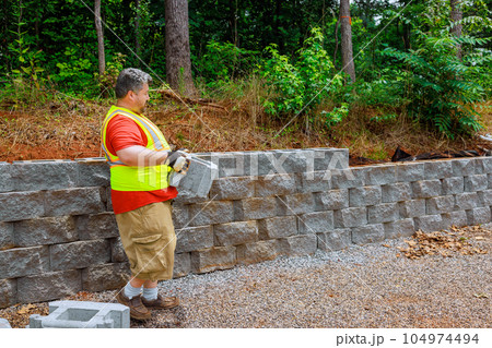 Construction worker mounting concrete block was perfectly aligned on retaining wall. 104974494