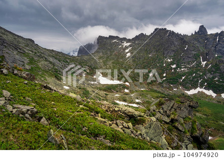 Green highland plateau against the background of rainy and foggy hills. Wild rainy nature of the Western Sayans. 104974920