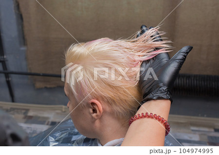 The hand of a girl of an experienced hairdresser in a black glove checks the degree of hair coloring, of an adult client in the salon The hand of a girl of an experienced hairdresser in a black glove checks the degree of hair coloring, of an adult client in the salon 104974995