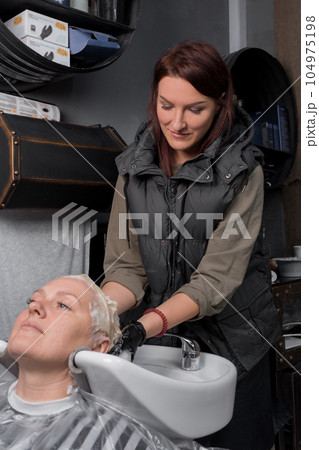 Smiling friendly beautiful brunette caucasian professional hairdresser in the process of washing the hair of a client at work Smiling friendly beautiful brunette caucasian professional hairdresser in the process of washing the hair of a client at work 104975198