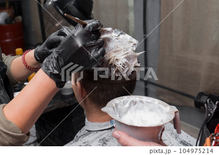 The process of dyeing a guy's client's hair white at work in a barbershop close-up 104975214