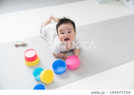 自然光が入るリビングのプレイマットで知育おもちゃを使って遊ぶご機嫌笑顔な生後8か月の赤ちゃん	 104975556