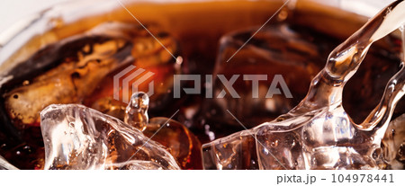 Pouring of Cola and Ice. Cola soda and ice splashing fizzing or floating up to top of surface. Close up of ice in cola water. Texture of carbonate drink with bubbles in glass. Cold drink background 104978441