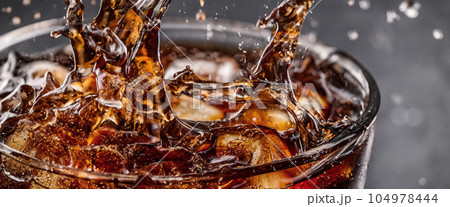 Pouring of Cola and Ice. Cola soda and ice splashing fizzing or floating up to top of surface. Close up of ice in cola water. Texture of carbonate drink with bubbles in glass. Cold drink background 104978444