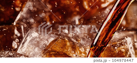 Pouring of Cola and Ice. Cola soda and ice splashing fizzing or floating up to top of surface. Close up of ice in cola water. Texture of carbonate drink with bubbles in glass. Cold drink background Pouring of Cola and Ice. Cola soda and ice splashing fizzing or floating up to top of surface. Close up of ice in cola water. Texture of carbonate drink with bubbles in glass. Cold drink background 104978447