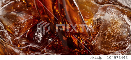 Pouring of Cola and Ice. Cola soda and ice splashing fizzing or floating up to top of surface. Close up of ice in cola water. Texture of carbonate drink with bubbles in glass. Cold drink background Pouring of Cola and Ice. Cola soda and ice splashing fizzing or floating up to top of surface. Close up of ice in cola water. Texture of carbonate drink with bubbles in glass. Cold drink background 104978448