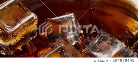 Pouring of Cola and Ice. Cola soda and ice splashing fizzing or floating up to top of surface. Close up of ice in cola water. Texture of carbonate drink with bubbles in glass. Cold drink background Pouring of Cola and Ice. Cola soda and ice splashing fizzing or floating up to top of surface. Close up of ice in cola water. Texture of carbonate drink with bubbles in glass. Cold drink background 104978449