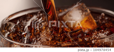 Pouring of Cola and Ice. Cola soda and ice splashing fizzing or floating up to top of surface. Close up of ice in cola water. Texture of carbonate drink with bubbles in glass. Cold drink background 104978454