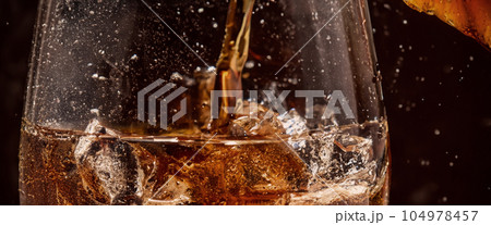 Pouring of Cola and Ice. Cola soda and ice splashing fizzing or floating up to top of surface. Close up of ice in cola water. Texture of carbonate drink with bubbles in glass. Cold drink background Pouring of Cola and Ice. Cola soda and ice splashing fizzing or floating up to top of surface. Close up of ice in cola water. Texture of carbonate drink with bubbles in glass. Cold drink background 104978457