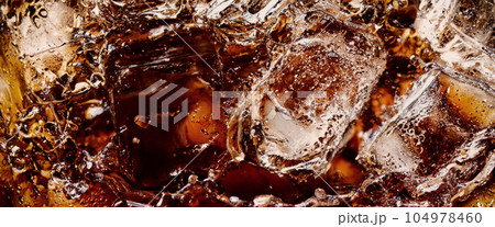 Pouring of Cola and Ice. Cola soda and ice splashing fizzing or floating up to top of surface. Close up of ice in cola water. Texture of carbonate drink with bubbles in glass. Cold drink background Pouring of Cola and Ice. Cola soda and ice splashing fizzing or floating up to top of surface. Close up of ice in cola water. Texture of carbonate drink with bubbles in glass. Cold drink background 104978460