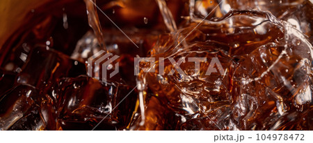 Pouring of Cola and Ice. Cola soda and ice splashing fizzing or floating up to top of surface. Close up of ice in cola water. Texture of carbonate drink with bubbles in glass. Cold drink background 104978472