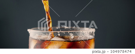 Pouring of Cola and Ice. Cola soda and ice splashing fizzing or floating up to top of surface. Close up of ice in cola water. Texture of carbonate drink with bubbles in glass. Cold drink background Pouring of Cola and Ice. Cola soda and ice splashing fizzing or floating up to top of surface. Close up of ice in cola water. Texture of carbonate drink with bubbles in glass. Cold drink background 104978474