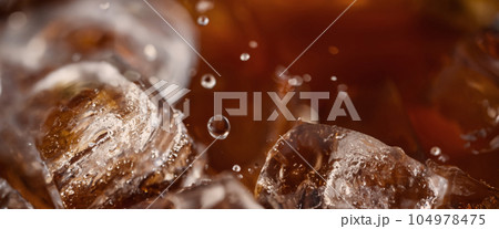 Pouring of Cola and Ice. Cola soda and ice splashing fizzing or floating up to top of surface. Close up of ice in cola water. Texture of carbonate drink with bubbles in glass. Cold drink background Pouring of Cola and Ice. Cola soda and ice splashing fizzing or floating up to top of surface. Close up of ice in cola water. Texture of carbonate drink with bubbles in glass. Cold drink background 104978475