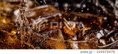 Pouring of Cola and Ice. Cola soda and ice splashing fizzing or floating up to top of surface. Close up of ice in cola water. Texture of carbonate drink with bubbles in glass. Cold drink background Pouring of Cola and Ice. Cola soda and ice splashing fizzing or floating up to top of surface. Close up of ice in cola water. Texture of carbonate drink with bubbles in glass. Cold drink background 104978476