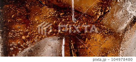Pouring of Cola and Ice. Cola soda and ice splashing fizzing or floating up to top of surface. Close up of ice in cola water. Texture of carbonate drink with bubbles in glass. Cold drink background Pouring of Cola and Ice. Cola soda and ice splashing fizzing or floating up to top of surface. Close up of ice in cola water. Texture of carbonate drink with bubbles in glass. Cold drink background 104978480