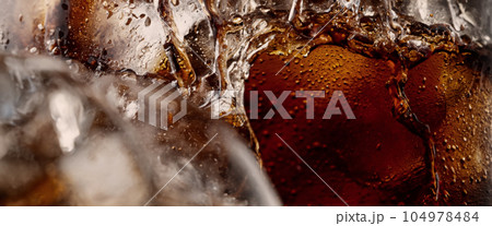 Pouring of Cola and Ice. Cola soda and ice splashing fizzing or floating up to top of surface. Close up of ice in cola water. Texture of carbonate drink with bubbles in glass. Cold drink background Pouring of Cola and Ice. Cola soda and ice splashing fizzing or floating up to top of surface. Close up of ice in cola water. Texture of carbonate drink with bubbles in glass. Cold drink background 104978484