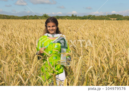 Girl waving flag of Pakistan outdoors over blue cloudy sky and golden wheat. 104979576