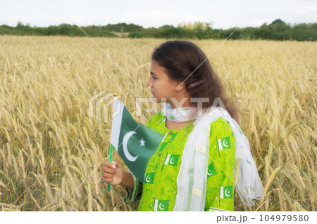 Girl waving flag of Pakistan outdoors over blue cloudy sky and golden wheat. 104979580