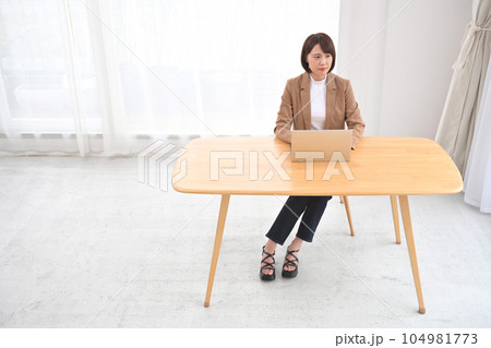 屋内の木製の机でノートパソコンの操作をする女性 屋内の木製の机でノートパソコンの操作をする女性 104981773