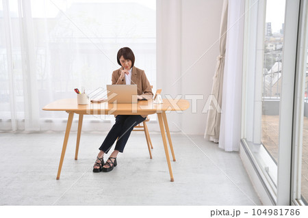 屋内の木製の机でノートパソコンの操作をする女性 屋内の木製の机でノートパソコンの操作をする女性 104981786