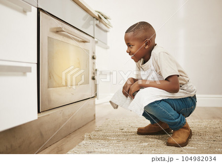 Cant wait to taste these. Shot of a little boy watching his baked goods cook in the oven at home. Cant wait to taste these. Shot of a little boy watching his baked goods cook in the oven at home. 104982034