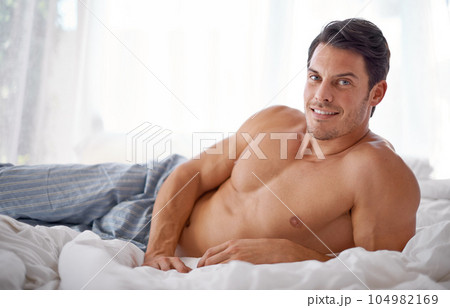 Sexy, smile and portrait of a man on a bed for relaxing, comfort and rest in pyjamas. Comfy, cozy and handsome young man content in the bedroom, smiling and confident to relax on the weekend Sexy, smile and portrait of a man on a bed for relaxing, comfort and rest in pyjamas. Comfy, cozy and handsome young man content in the bedroom, smiling and confident to relax on the weekend 104982169