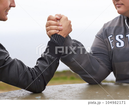 Hands, friends and competition with men and arm wrestling in nature for challenge, power and respect. Team, strong and conflict with closeup of people and holding hands for muscle, match and rival Hands, friends and competition with men and arm wrestling in nature for challenge, power and respect. Team, strong and conflict with closeup of people and holding hands for muscle, match and rival 104982171