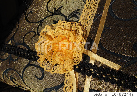A beautiful yellow-orange lace artificial flower sewn onto a decorative cushion satin fabric. Blue dense braid with thin polyester lace. Decoration of decorative pillowcases. Women's needlework 104982445