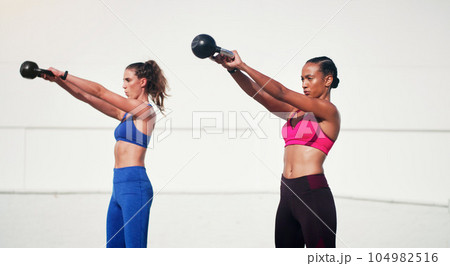 Woman, personal trainer and kettlebell in weightlifting for workout, exercise or fitness together outdoors. Women lifting kettle bells for exercising, strength or training body in health and wellness 104982516