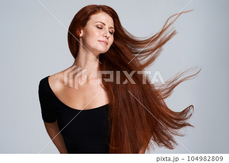 Hair, beauty and woman in studio with wind for keratin treatment, wellness and haircare on gray background. Salon, hairdresser and face of ginger female model for shine, healthy and natural hairstyle 104982809