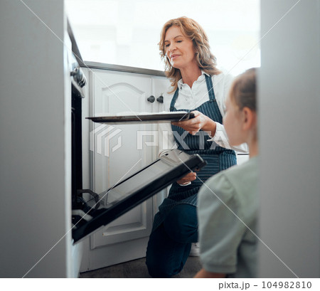 These will bake quickly and then we can enjoy them. Shot of a grandmother inserting a tray into a hot oven while baking with her granddaughter at home. These will bake quickly and then we can enjoy them. Shot of a grandmother inserting a tray into a hot oven while baking with her granddaughter at home. 104982810