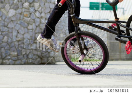 Legs, wheel and person on bicycle for trick, challenge and action at skatepark in city. Closeup, cycling stunt and urban biker in town with skill for balance, performance risk and freedom of motion 104982811