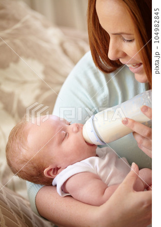 Mother, baby and feeding milk from bottle for nutrition, healthy breakfast and diet in the morning. Mom, child and feed newborn formula food for growth, development and wellness in happy home bedroom 104982845
