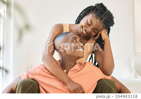 Young happy carefree and cheerful african american couple bonding and enjoying relaxing time together at home. Loving black female smiling while hugging and looking at her boyfriend sitting together 104983118