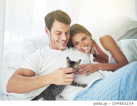 Bedroom love, pet cat and happy couple relax for morning peace, calm and bonding quality time together in Toronto Canada. Flare, animal kitten and romantic people smile in home bed for Valentines Day 104983254