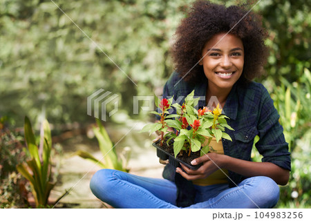 Black woman in garden, smile in portrait with gardening and plant or flower, botany and young gardener outdoor. Happy female person with growth, environment and plants out in nature with landscaping 104983256