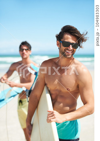 Beach, summer and man surfing friends outdoor together for travel, vacation or holiday trip overseas. Surf, sea or fun with a young male surfer in sunglasses and friend bonding on an ocean coast 104983303