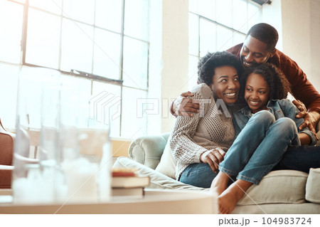 Love, bond and family hugging while relaxing together in the living room of their modern house. Happy, smile and African parents spending quality time, talking and hugging girl child on sofa at home. 104983724