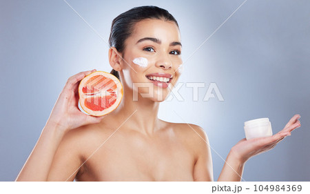 Skincare, face cream and woman with grapefruit in studio for a natural, organic or health facial routine. Beauty, self care and female model with citrus fruit and spf for treatment by gray background Skincare, face cream and woman with grapefruit in studio for a natural, organic or health facial routine. Beauty, self care and female model with citrus fruit and spf for treatment by gray background 104984369