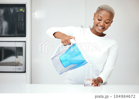 Water, filter and black woman with jug in kitchen to refresh with glass, liquid and cold hydration. Happy, thirsty and female person pouring pure aqua beverage from pitcher for clean drinking at home 104984672