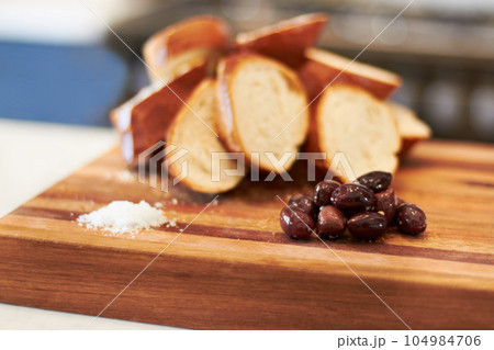Olives, food and bakery with bread in kitchen for nutrition, health and diet. Breakfast, cafe and coffee shop with closeup of product on cutting board on table for wheat, grain and cooking 104984706