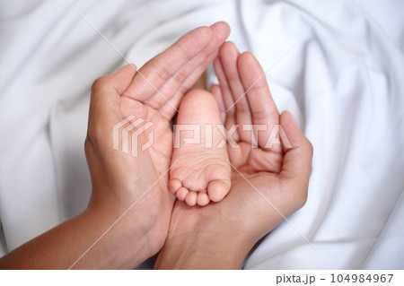 Hands, newborn and closeup of a baby foot with mother holding for care, love and nurture. Childcare, cute and zoom of a woman with her infant child feet in the crib of nursery at their family home. Hands, newborn and closeup of a baby foot with mother holding for care, love and nurture. Childcare, cute and zoom of a woman with her infant child feet in the crib of nursery at their family home. 104984967