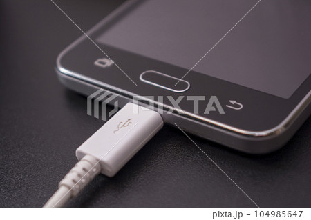 black smartphone on black background with white cable black smartphone on black background with white cable 104985647