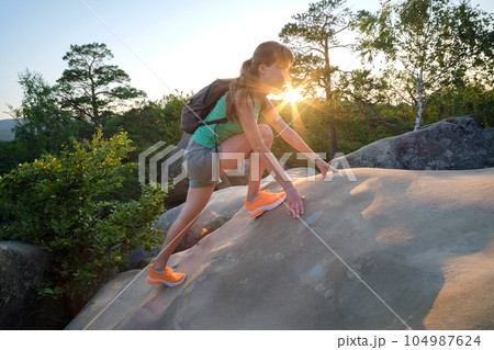 Young woman climbing alone on rocky mountain path. Female hiker enjoying difficult challenge on wilderness trail. Active way of life concept 104987624